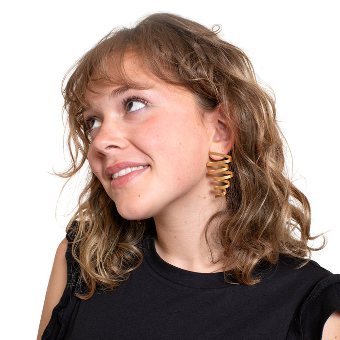 Woman wearing gold spiral earrings on a white background