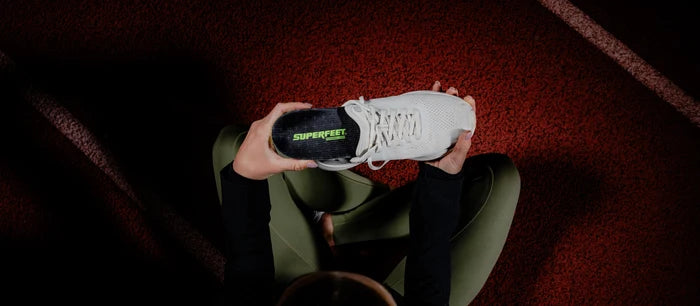 Person holding a white sneaker while putting in Superfeet's ME3D Personalized Insole.