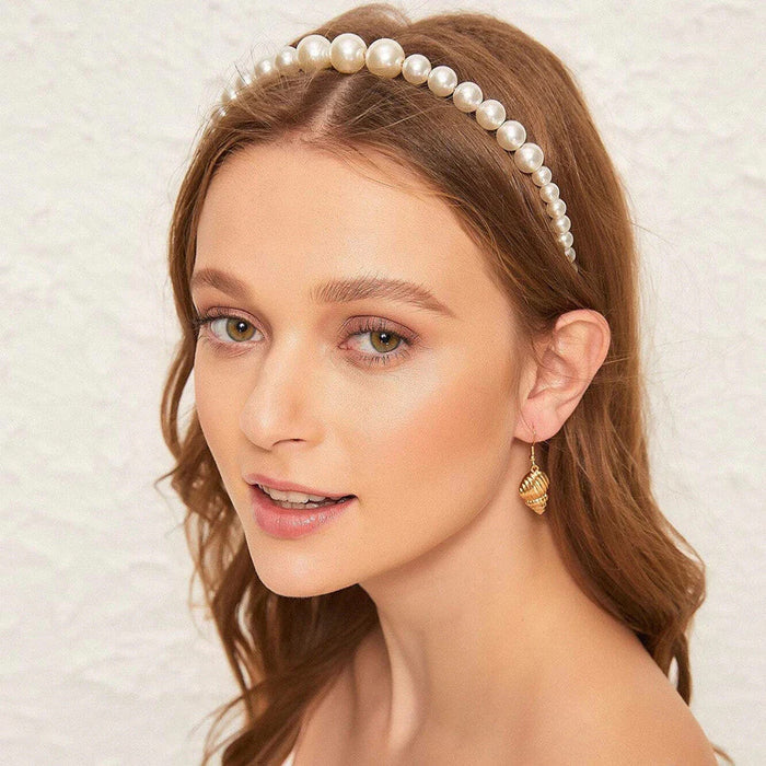 Woman wearing a pearl headband and gold earrings against a neutral background