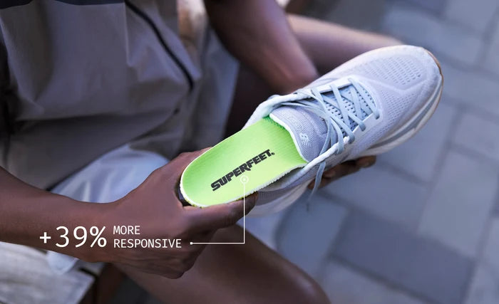 Person inserting Superfeet's Run Pacer Elite insole into a light gray athletic shoe inserting. Text reading "+39% More Responsive".