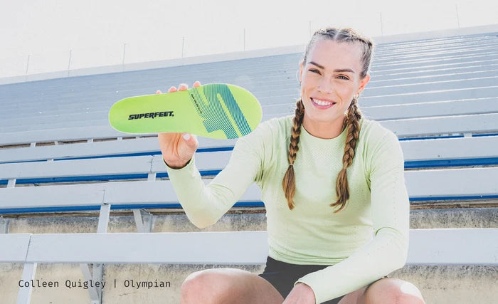 U.S.A's Olympian Colleen Quigley holding Superfeet's Run Pacer Elite insole while sitting outside on a stadium bench.