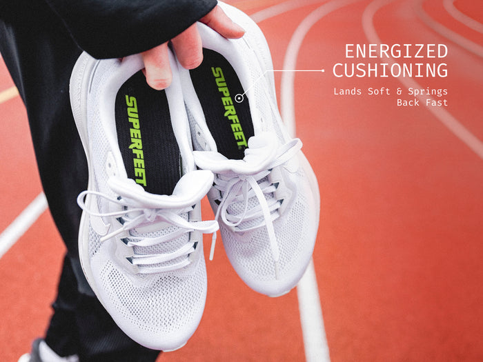 Someone standing on a track holding Superfeet's Run Pacer Insole inside of a white running shoe. Text Reads "Energized Cushioning Land Soft & Springs Back Fast"