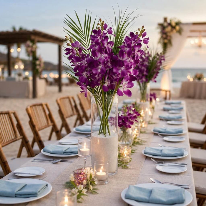 Purple silk vanda orchid sprays in a tall glass vase on a beachside wedding table
