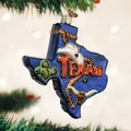 A Texas-shaped Christmas ornament on a tree, decorated with a cactus, cowboy hat, longhorn skull, and the word TEXAS in bold red letters.